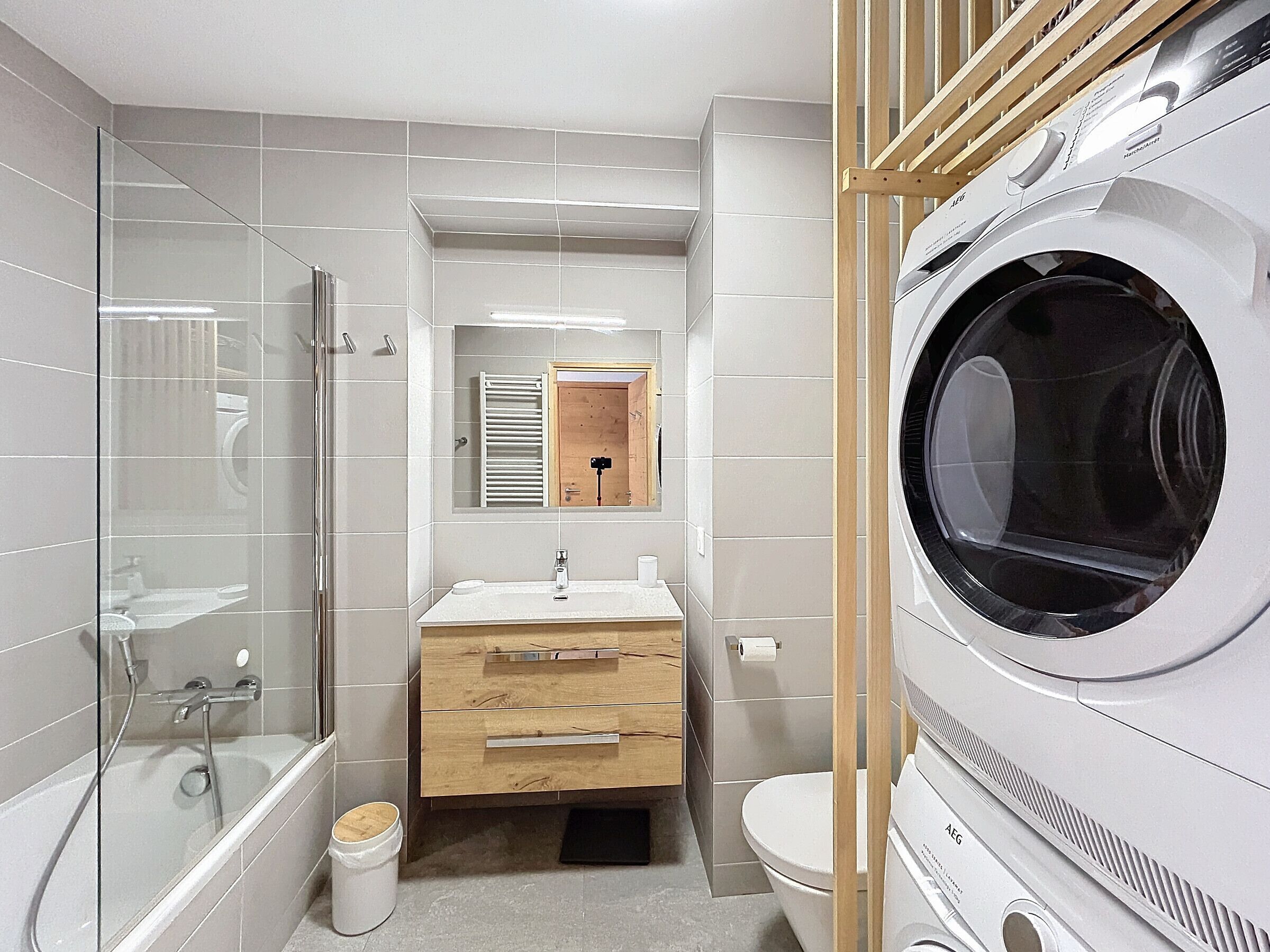 Une salle de bain moderne avec une douche à parois de verre, un meuble-lavabo en bois, des toilettes et un lave-linge à chargement frontal.