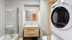 Un baño moderno con cabina de ducha de vidrio, tocador de madera, inodoro y lavadora de carga frontal.