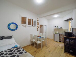 A compact room with a bed, a dining table with chairs, a kitchenette, and a small TV.