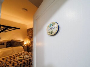 A hotel room with a bed, a wall-mounted sign, and a stone wall.