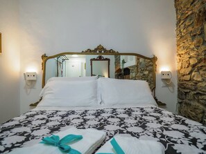 Una cama con una colcha estampada, un espejo con un marco decorativo y una pared de piedra.