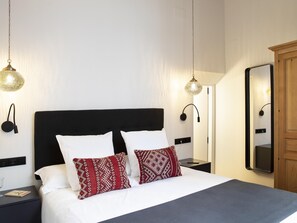 A neatly made bed with white and patterned pillows, a black headboard, and two bedside tables with lamps.