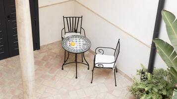 A small patio area with a tiled floor, a round table with a yellow object on it, two metal chairs, and a potted plant.