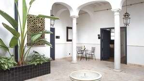 Un cortile con una fontana, piante in vaso, un tavolo con sedie e un muro decorato.