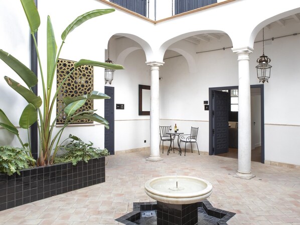 Ein Innenhof mit Brunnen, Topfpflanzen, einem Tisch mit Stühlen und einer Wand mit Muster.