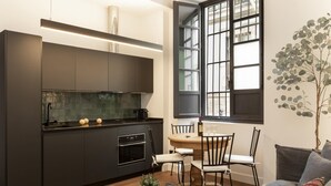 Una cucina moderna con mobili scuri, forno integrato e macchina da caffè. C'è un'area pranzo con tavolo e sedie, e un'ampia finestra con vista sulla città.