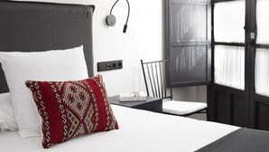 Ein modernes Hotelzimmer mit einem großen Bett, einem Nachttisch, einem Sessel, einer Wandlampe und einem Fenster mit Vorhängen.