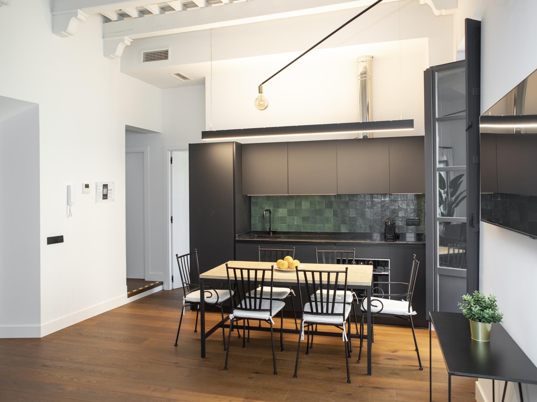 Una cucina moderna con mobili scuri, un'isola centrale e un'area pranzo con tavolo e sedie in legno.