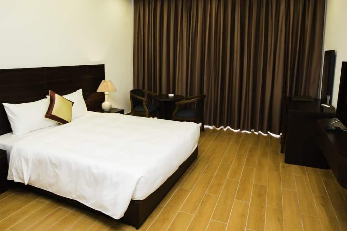 A hotel room with a large bed, a desk, a chair, a lamp, and a TV.