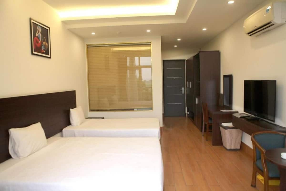 A hotel room with a bed, a desk, a television, and a window with blinds.
