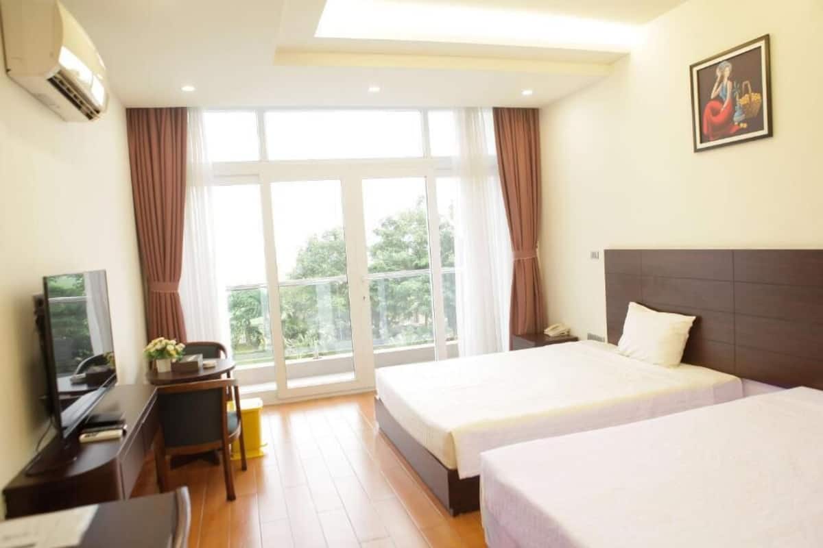A hotel room with two beds, a desk with a chair, a television, and a large window with curtains.