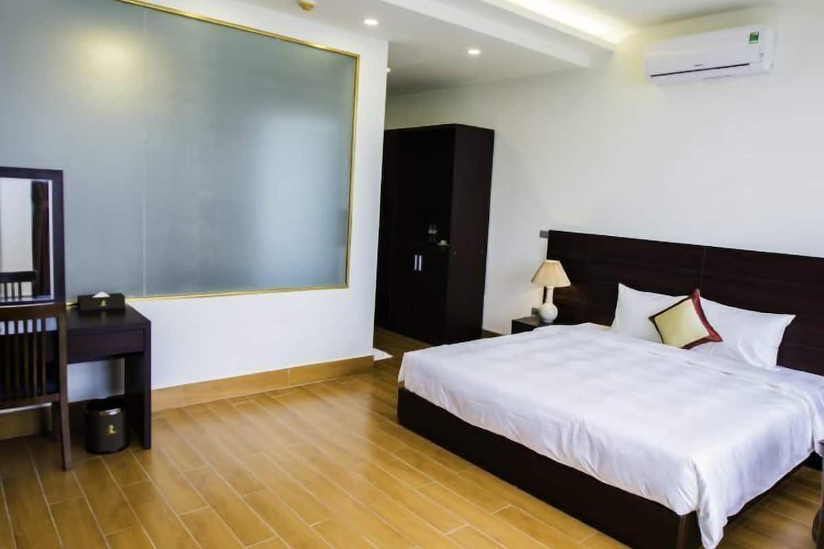 A modern hotel room with a large bed, a desk, and a wardrobe.