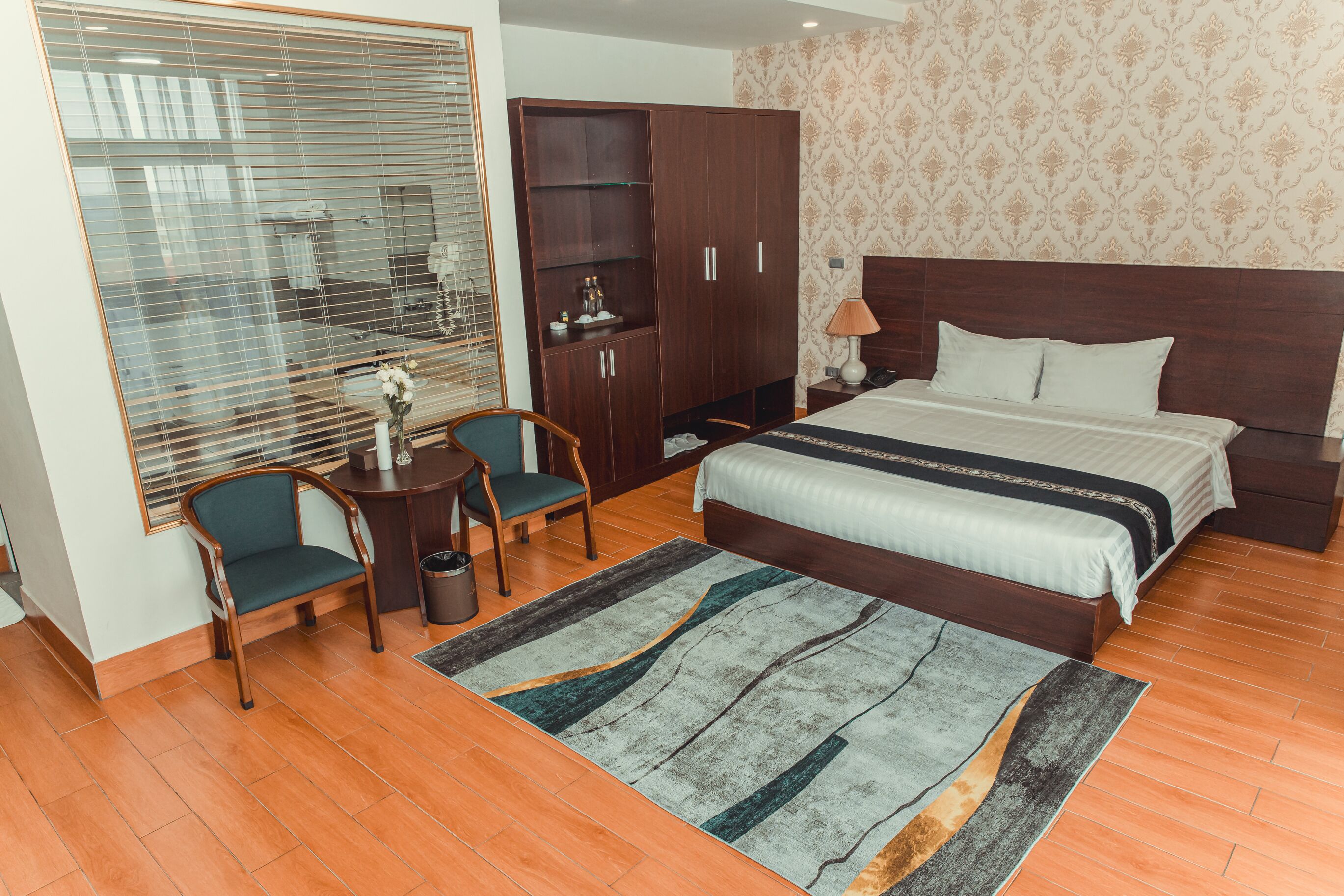Habitación de hotel con cama, armario, escritorio con silla, una mesita y ventana con persianas.