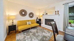 A living room with a yellow sofa, a fireplace, a rug, and a table with chairs. - Spacious 4/2BR Home |Pet-Friendly |Midtown Tulsa (Tulsa)
