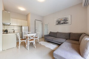 A compact living space with a kitchenette, a grey sofa, and a dining area with white chairs.
