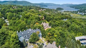 Een groot huis omgeven door dicht bos, met een meer en bergen op de achtergrond.