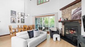 Een moderne woonkamer met een open haard, een eethoek met houten meubels en een groot raam met uitzicht op groen.