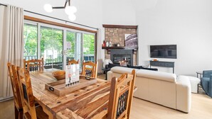 Een moderne woonkamer met een open haard, een eethoek met houten meubels en een televisie aan de muur.