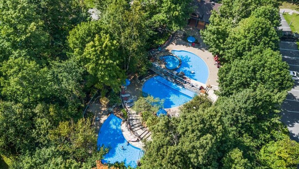 Luchtbeeld van een resort met meerdere zwembaden, omgeven door weelderige begroeiing.