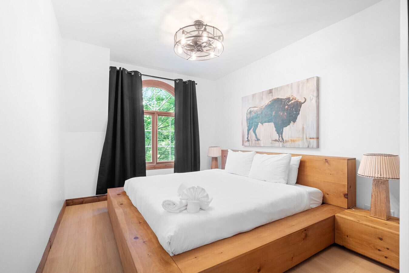 Une chambre avec un lit en bois, une fenêtre avec des rideaux noirs, une lampe fixée au mur et un tableau représentant un taureau.
