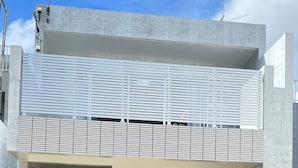 Um edifício moderno com fachada de concreto, varanda de metal e entrada protegida por portão.