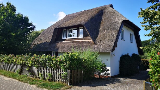 A traditional thatched-roof house with a white exterior, a wooden fence, and a paved driveway. - Vacation apartment in the countryside between Binz and Sellin (Zirkow)