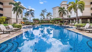 A swimming pool with lounge chairs and palm trees, surrounded by hotel buildings. - Hale Pikake O-406 Comfort and Joy in one place (Kapolei)