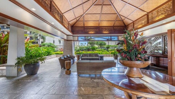 A spacious lobby with a high ceiling, a central seating area, and a view of the surrounding buildings. - Hale Pikake O-406 Comfort and Joy in one place (Kapolei)
