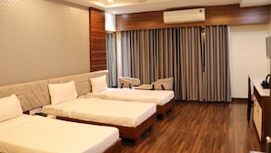 A hotel room with three beds, a desk, a chair, and a TV. - Hotel Manglam (Pachpadra)