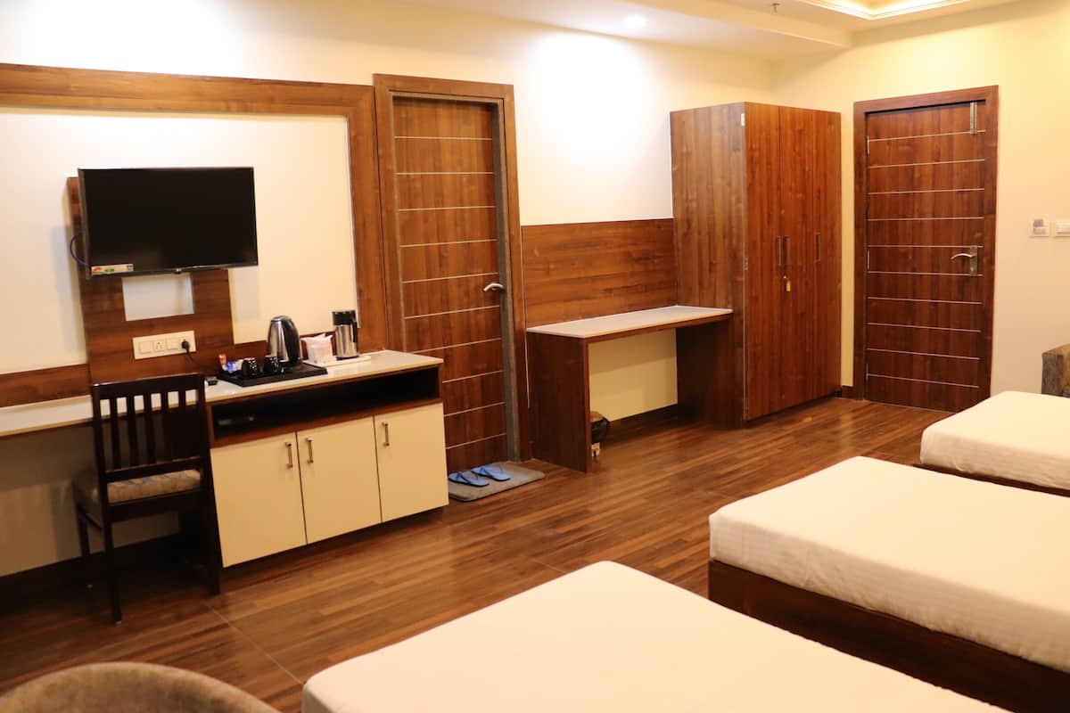 Quarto de hotel com piso de madeira, TV de tela plana na parede, escrivaninha com cadeira, duas camas de solteiro e um guarda-roupa.