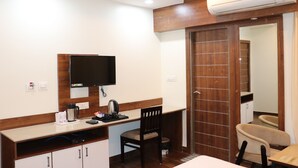 A hotel room with a kitchenette, a flat-screen TV, a wooden chair, a wooden desk, and a large mirror. - Hotel Manglam (Pachpadra)