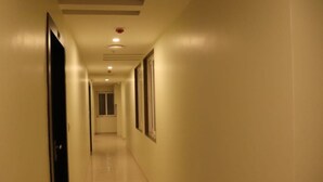 A long, narrow hallway with a tiled floor and light-colored walls. - Hotel Manglam (Pachpadra)