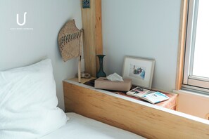 Habitación de hotel con cabecera de madera, almohada blanca, cesta tejida, un jarrón, una foto enmarcada y una revista sobre la mesita de noche.