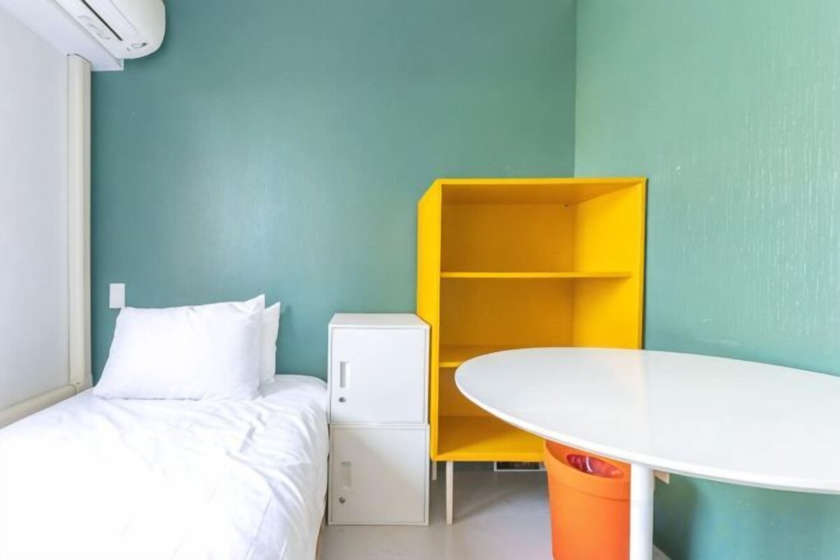 A room with a bed, a white table, and a yellow shelving unit.