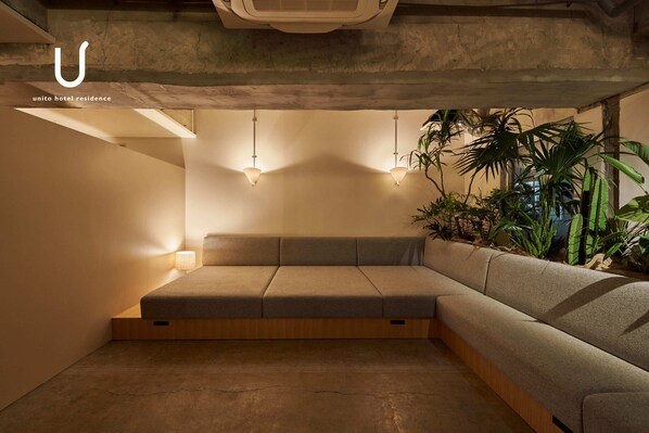 A modern hotel room with a built-in sofa, pendant lighting, and a concrete ceiling.