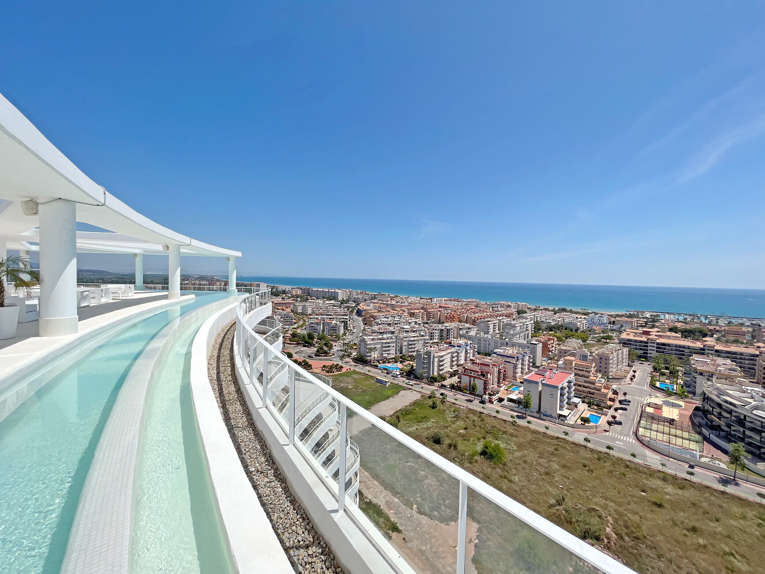 Un hotel moderno con piscina infinita en la azotea y vistas a una ciudad costera.