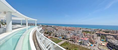 Un hotel moderno con piscina infinita en la azotea y vistas a una ciudad costera.