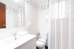 Un bagno con lavandino bianco, uno specchio, un WC e una tenda da doccia.