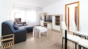 Ein modernes Wohnzimmer mit einer Couch, einem Glastisch, einem Fernseher und einem Essbereich mit Stühlen.