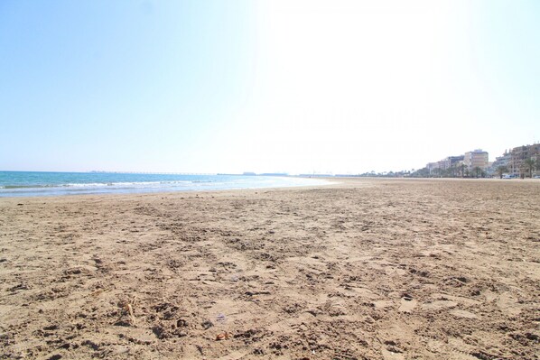 Ampia spiaggia sabbiosa con cielo sereno e vista sullo skyline costiero.