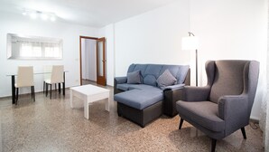 Ein Wohnzimmer mit einem Ecksofa, einem grauen Sessel, einem Couchtisch und einem Glastisch mit Stühlen.