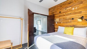 Moderni hotellihuone, jossa on puukoristeinen seinä, suuri sänky valkoisilla vuodevaatteilla, pieni työpöytä ja tuoli.