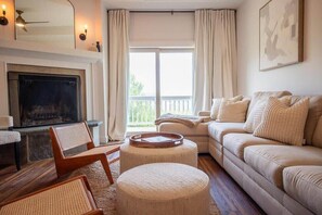A living room with a fireplace, a sofa, two chairs, a coffee table, and a balcony with curtains. - Mountainside 2-BR Ski-In/Out Okemo Haven (Ludlow)
