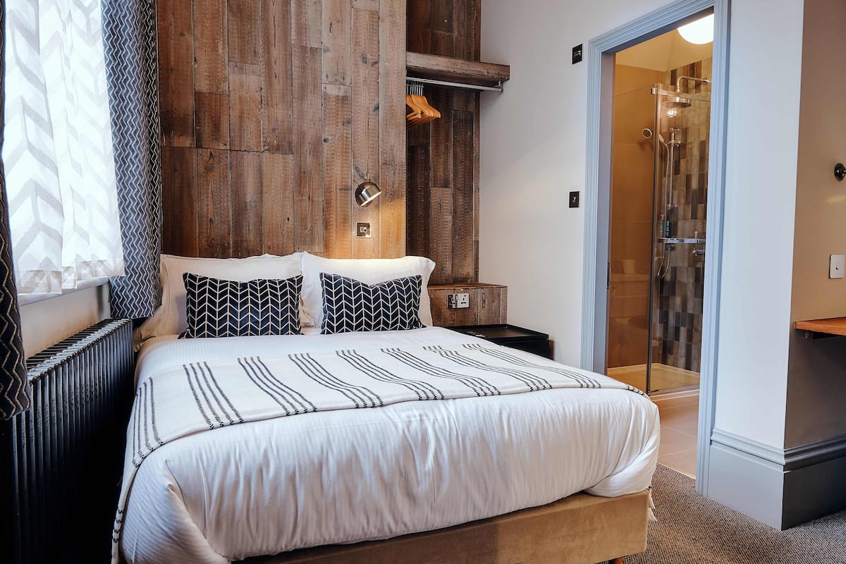 Quarto com uma cama grande, painel de parede de madeira e área de chuveiro envidraçada.