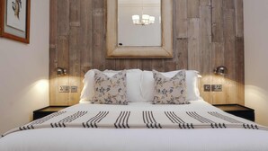 Una cama bien hecha con una colcha estampada, un cabecero de madera con un espejo y dos lámparas de noche.