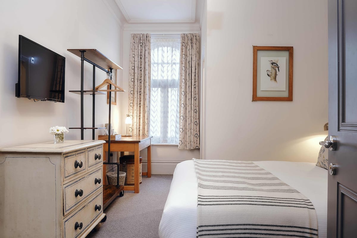 Quarto com cama, penteadeira, escrivaninha, televisão e janela com cortinas.
