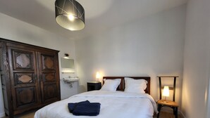 A bedroom with a large bed, a wooden wardrobe, a bedside table with a lamp, and a wall-mounted mirror. - N°9, in the heart of the Haut Doubs tourist region, 10 minutes from Switzerland (Damprichard)