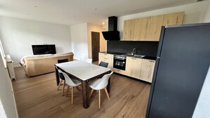 A modern kitchen with wooden cabinets, a black refrigerator, and a dining area with a table and chairs. - N°9, in the heart of the Haut Doubs tourist region, 10 minutes from Switzerland (Damprichard)