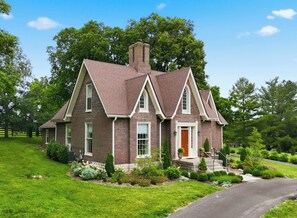 A two-story brick house with a gabled roof, a front porch, and a well-maintained lawn.