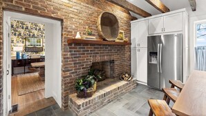 A kitchen with a brick fireplace, white cabinets, and a stainless steel refrigerator.